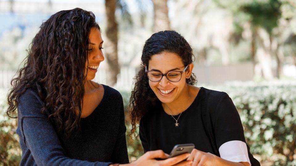 Dos mujeres al aire libre mirando un dispositivo móvil con tecnología de reconocimiento facial.