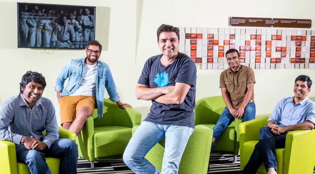 Five members of the InstaFact team pose on bright green chairs.