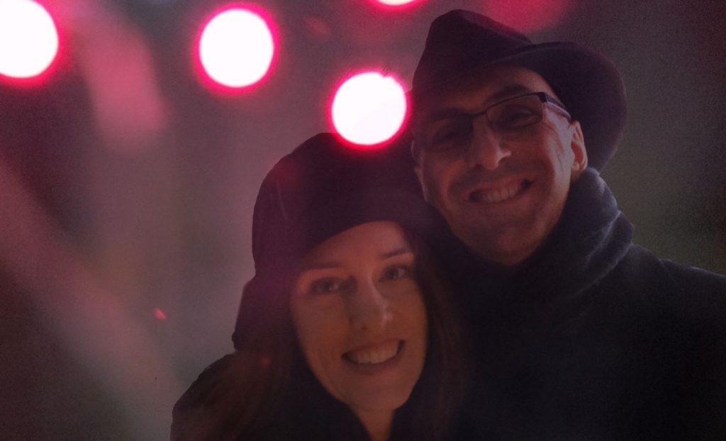 Jorge and Stephanie smile against a nighttime background dotted with red lights.