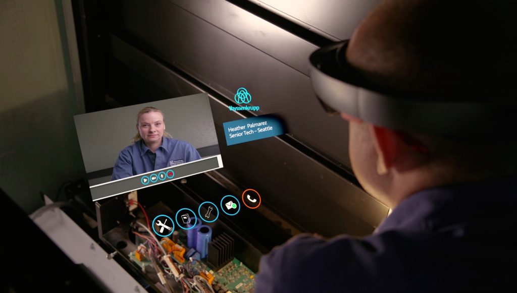 Elevator technician wearing HoloLens talks to a woman on Skype, who appears virtually in front of him