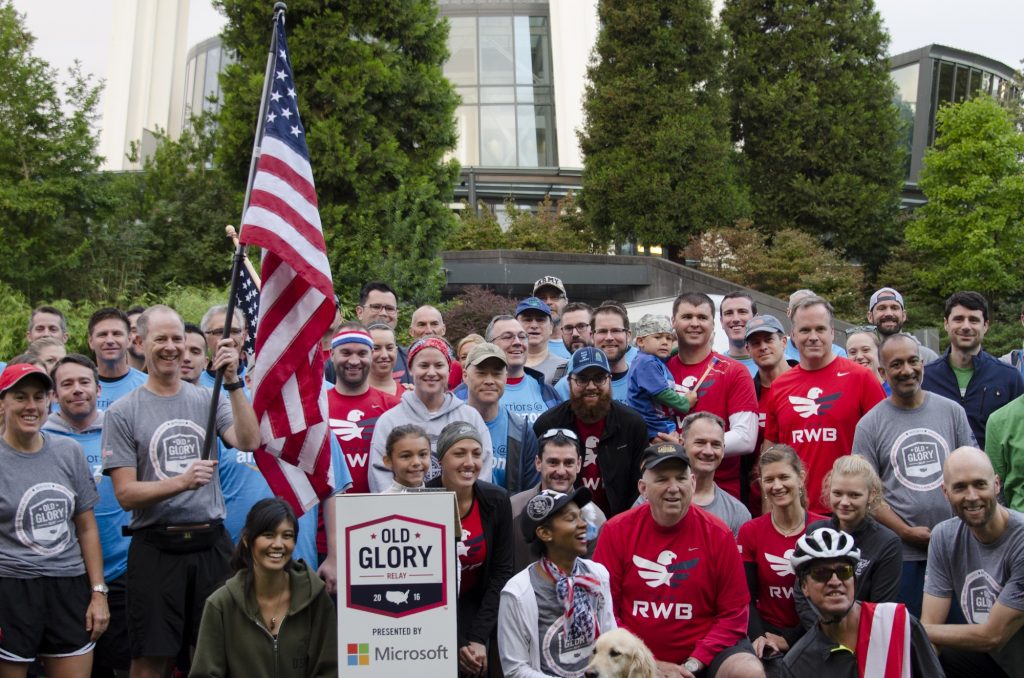 Group of people in running gear posed in front of the Space Needle with an American flag.