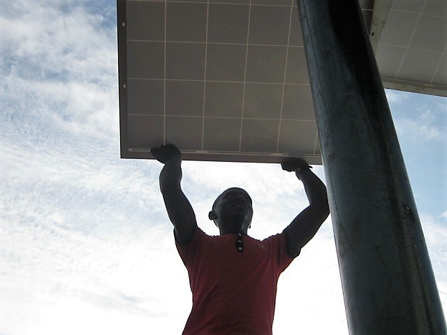 Phot of man outdoors installing micro-grid technology on one of Uganda’s Ssese Islands.