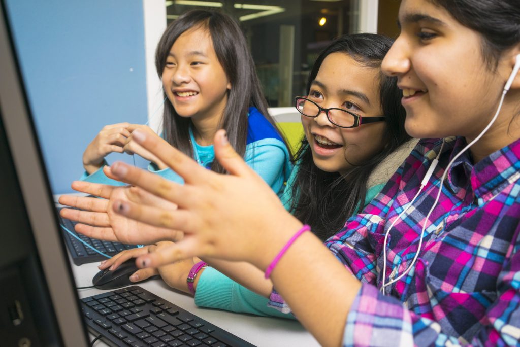 Photo of three smiling girls having an animated chat while working at a computer