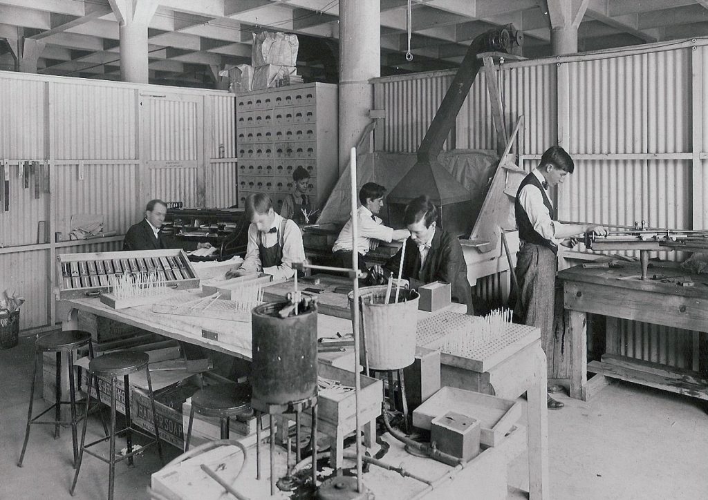 Old black and white photo shows workers manufacturing products by hand