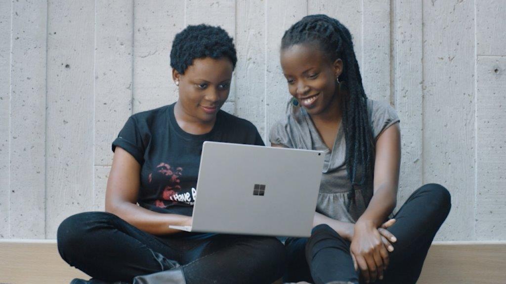 Two women sit together, looking at a laptop screen.