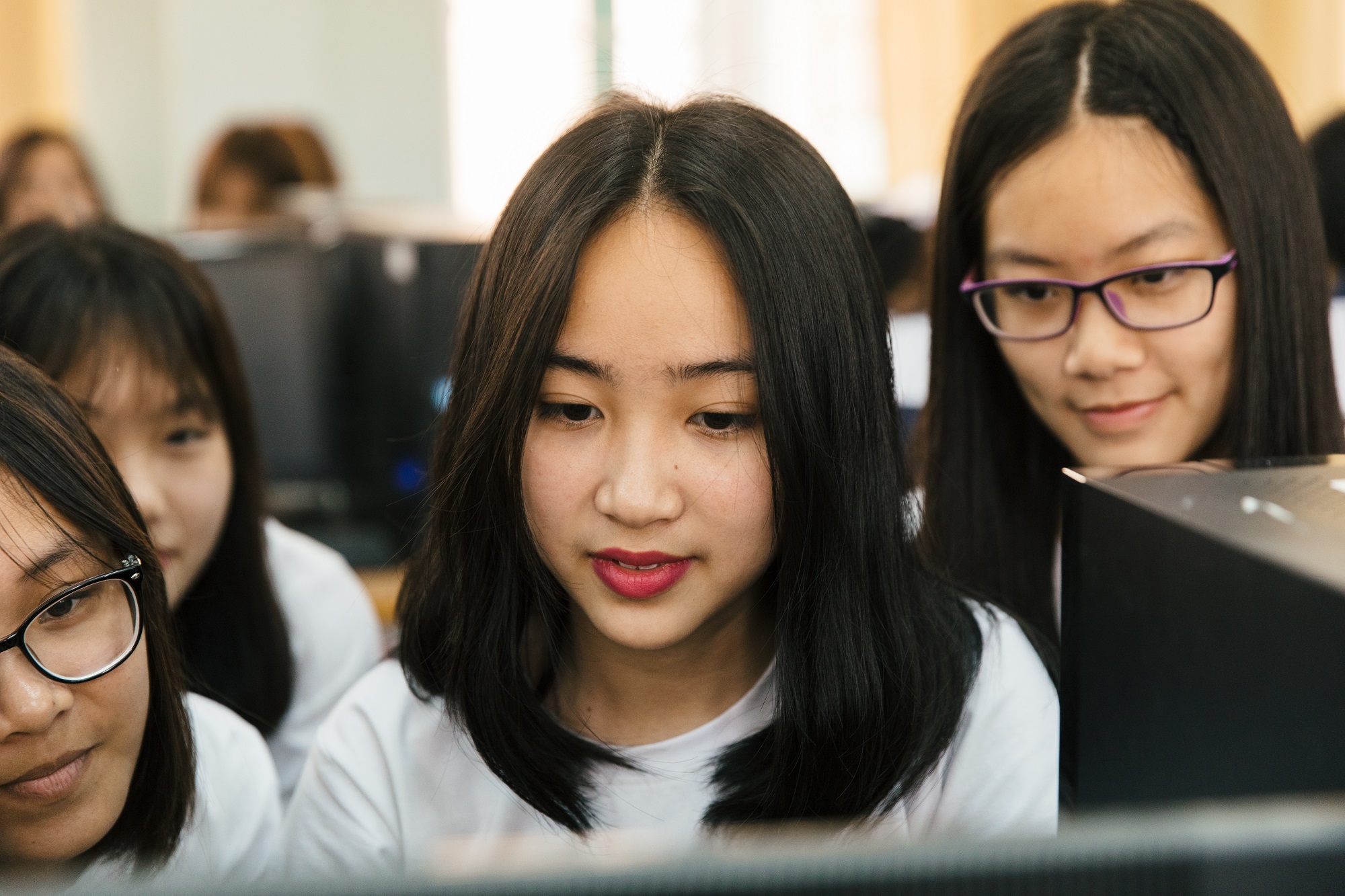Female students crowd around a computer screen, smiling