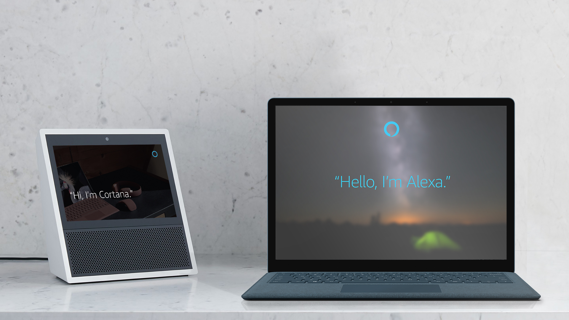 Photo shows the words “Hi, I’m Cortana” on the screen of an Amazon Echo Show device next to a laptop that displays the words “Hello, I’m Alexa”