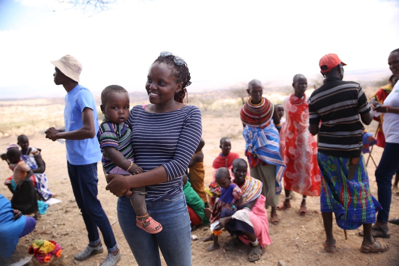 Verah Okeyo holding a baby among a crowd of people, including women and children, in Samburu County, Kenya.