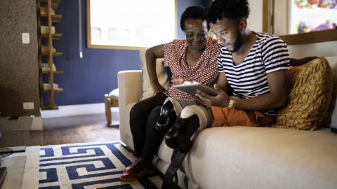 A grandmother and grandson, who has a physical disability, view a digital tablet while seated on a sofa in a home in Brazil.