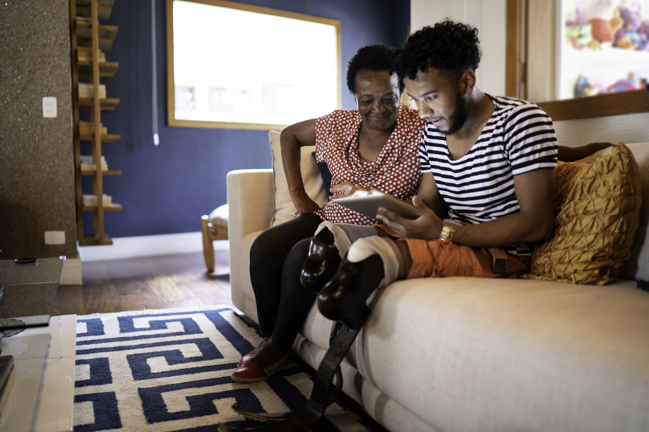 A grandmother and grandson, who has a physical disability, view a digital tablet while seated on a sofa in a home in Brazil.