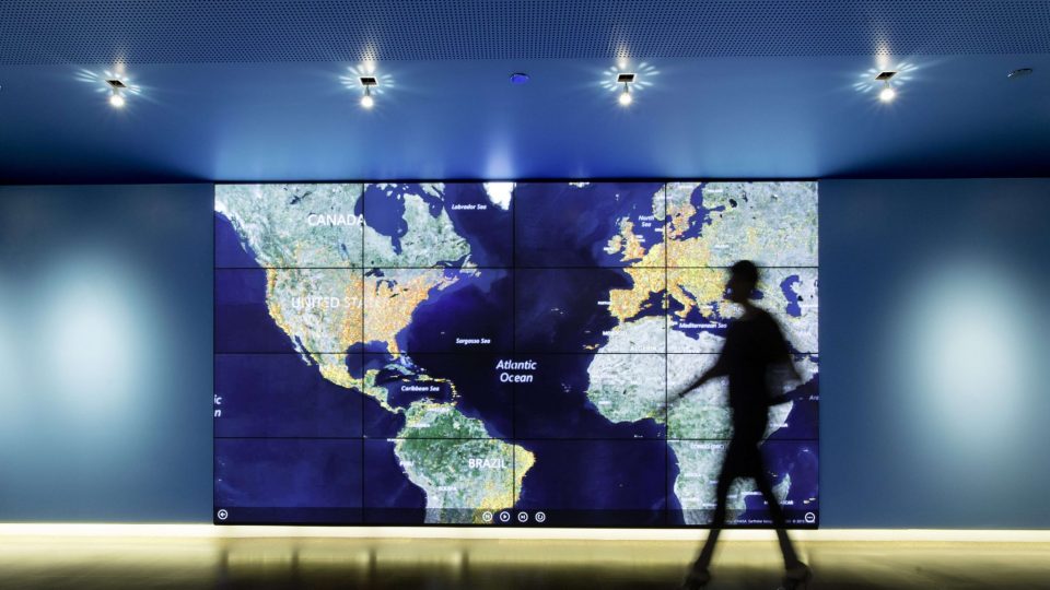 Silhouette of a person walking in front of an enlarged map of North, Central, and South America, Europe, and Africa.