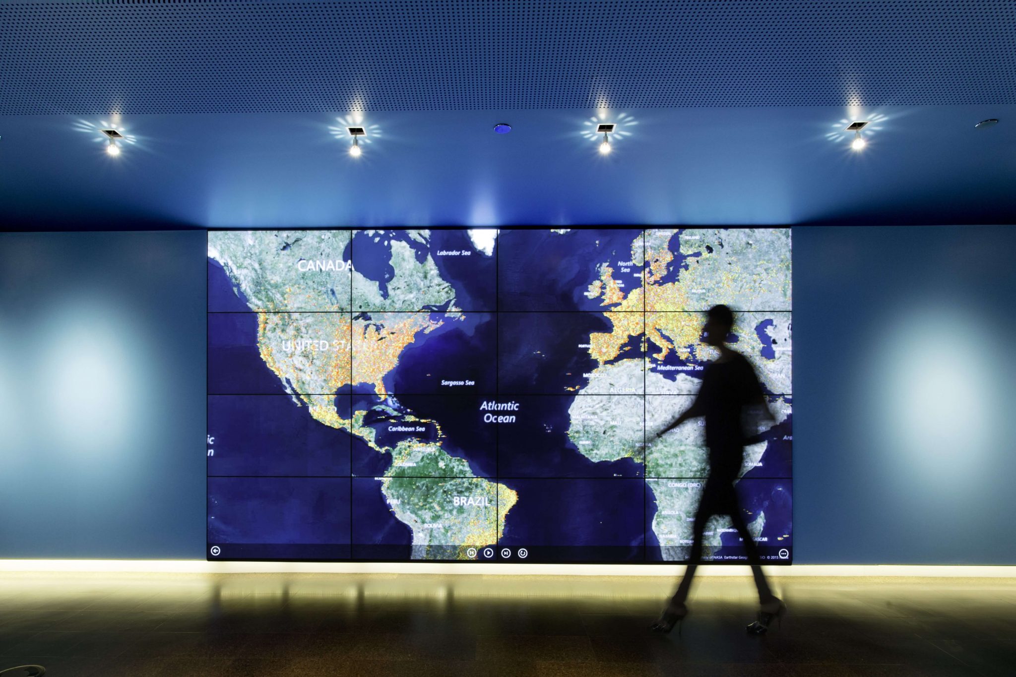 Silhouette of a person walking in front of an enlarged map of North, Central, and South America, Europe, and Africa.