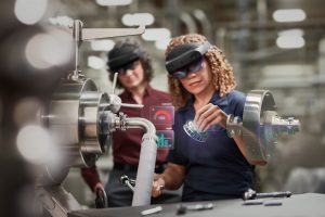 Two women in manufacturing plant using Microsoft Hololens 2 for assembly. Contains hologram scenario. Contains hologram. Contextual imagery.