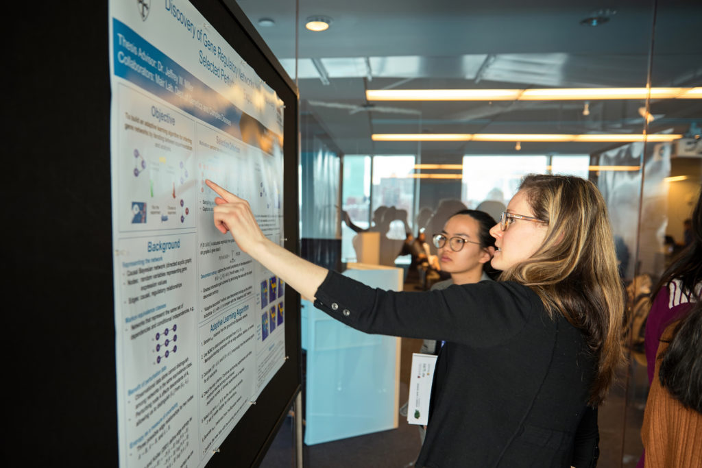 A data scientist at WiDS Cambridge explains a poster presentation to an attendee.