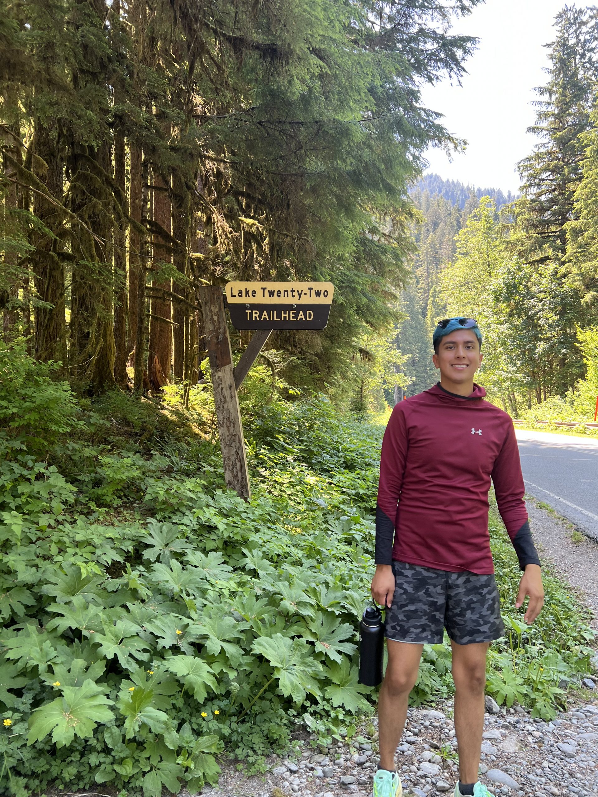 Alexis vistiendo ropa deportiva junto a un cartel que dice "Inicio del sendero del lago veintidós"