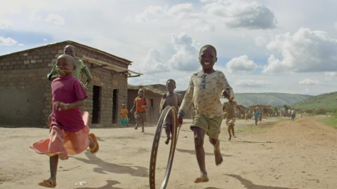 Children race a spinning wheel down a dirt road