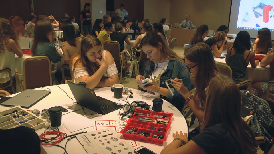 A group of teen girls sitting at a table work with computer parts at a Girls in AI Hackathon in Athens, Greece