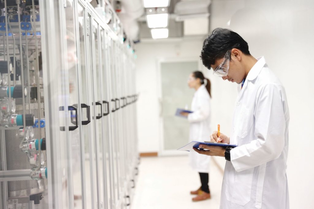 Two individuals in lab coats observe a factory