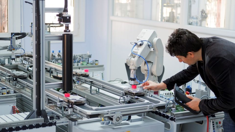 A worker adjusts a robotic arm in a factory setting