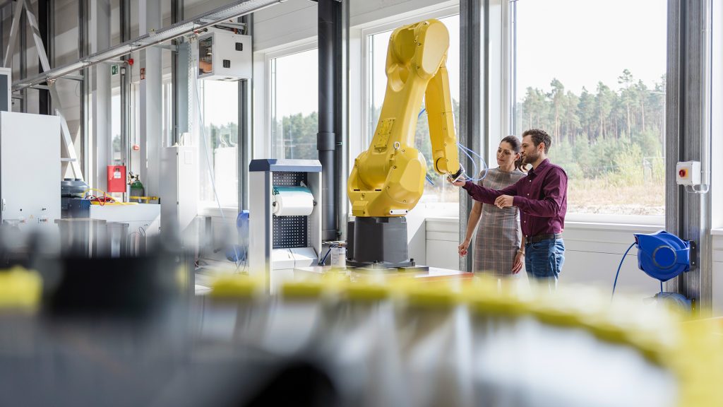 A man and a woman stand next to a robotic arm in an Industry 4.0 factory.