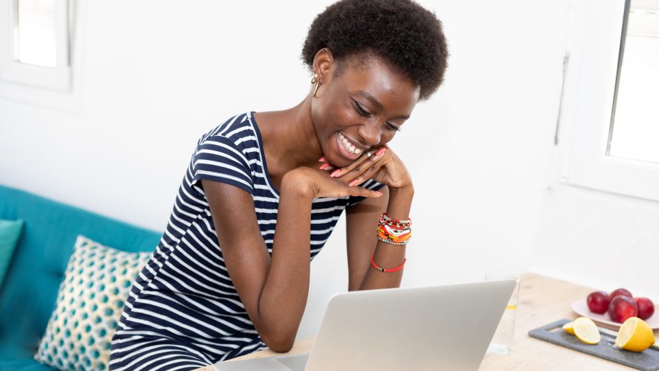 A smiling person sits in front of a laptop