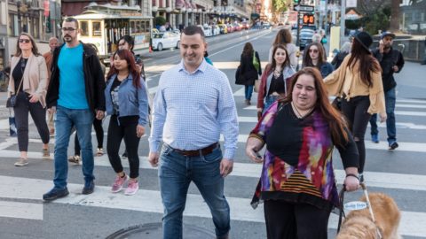 Image of Alex and Maia crossing a busy intersection in downtown San Francisco. Maia is using Soundscape which has given her information about the layout of the intersection in 3D audio