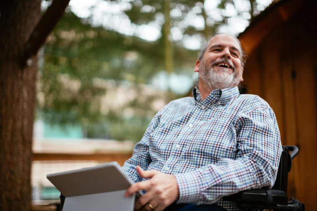 Stuart Pixley, a Senior Attorney at Microsoft who uses a wheelchair, smiles while holding a Surface