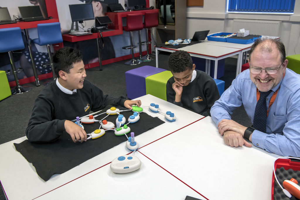 From the left, student Daniel and Rico and IT instructor Jonathon Fogg sit around a table and laugh about the program Daniel and Rico created during a beta test of the technology behind Code Jumper.