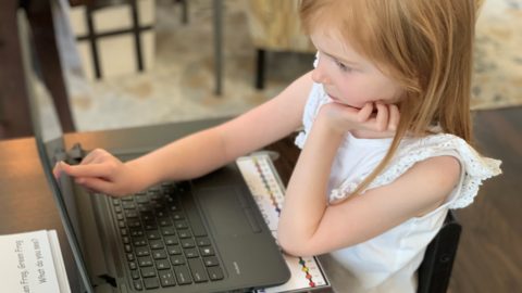 Kindergarten age girl touching a computer screen.