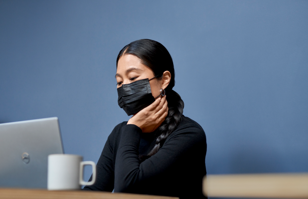 Woman wearing a mask looking pensively into her computer