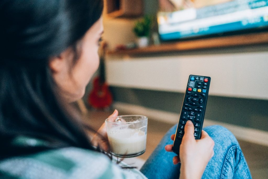 A person holding a remote and a coffee cup watching TV