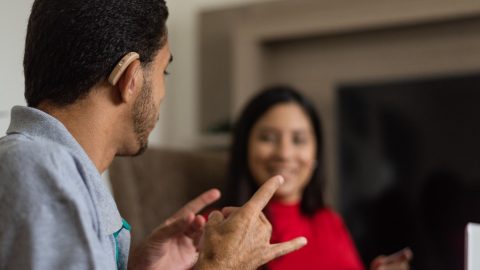Two people communicating through sign language one of which is wearing a hearing aid