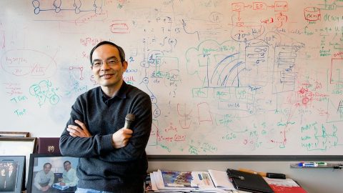 Xuedong Huang stands arms folded in front of a fully used whiteboard