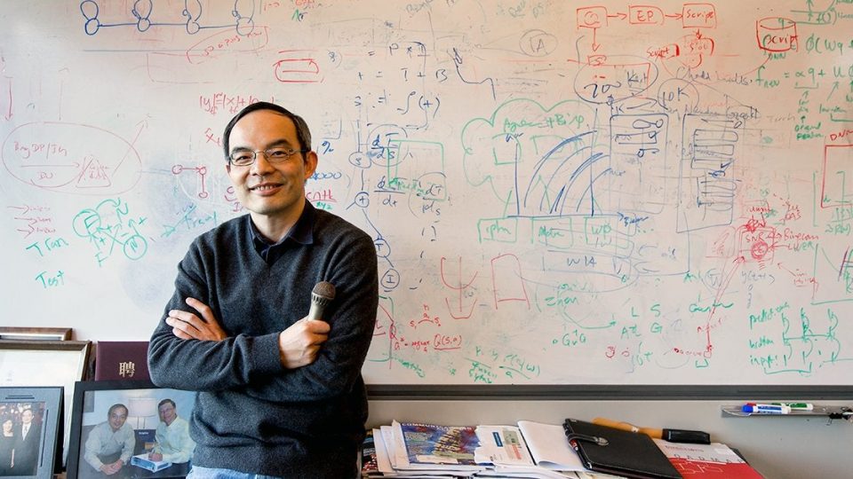 Xuedong Huang stands arms folded in front of a fully used whiteboard