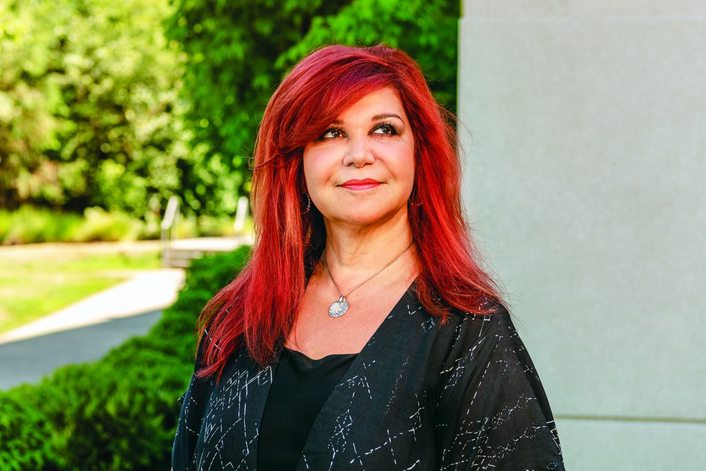 Photograph of Mitra Azizirad, with vibrant red hair, looking off into the distance. 