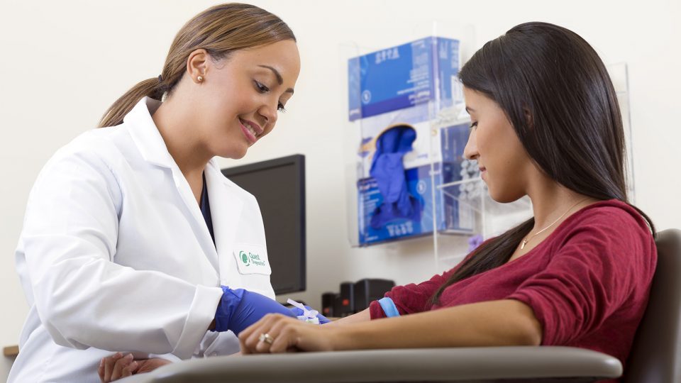 A female phlebotomist draws blood from a seated female patient