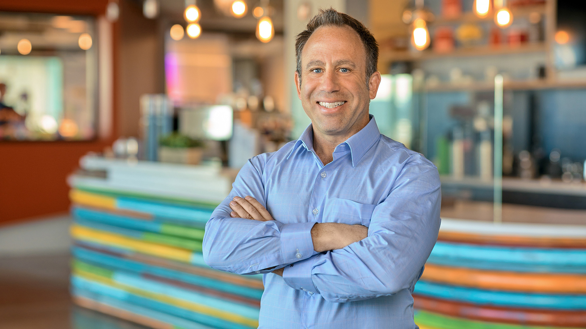 Dan Roth stands with arms folded in front of a counter with a colorful, striped pattern