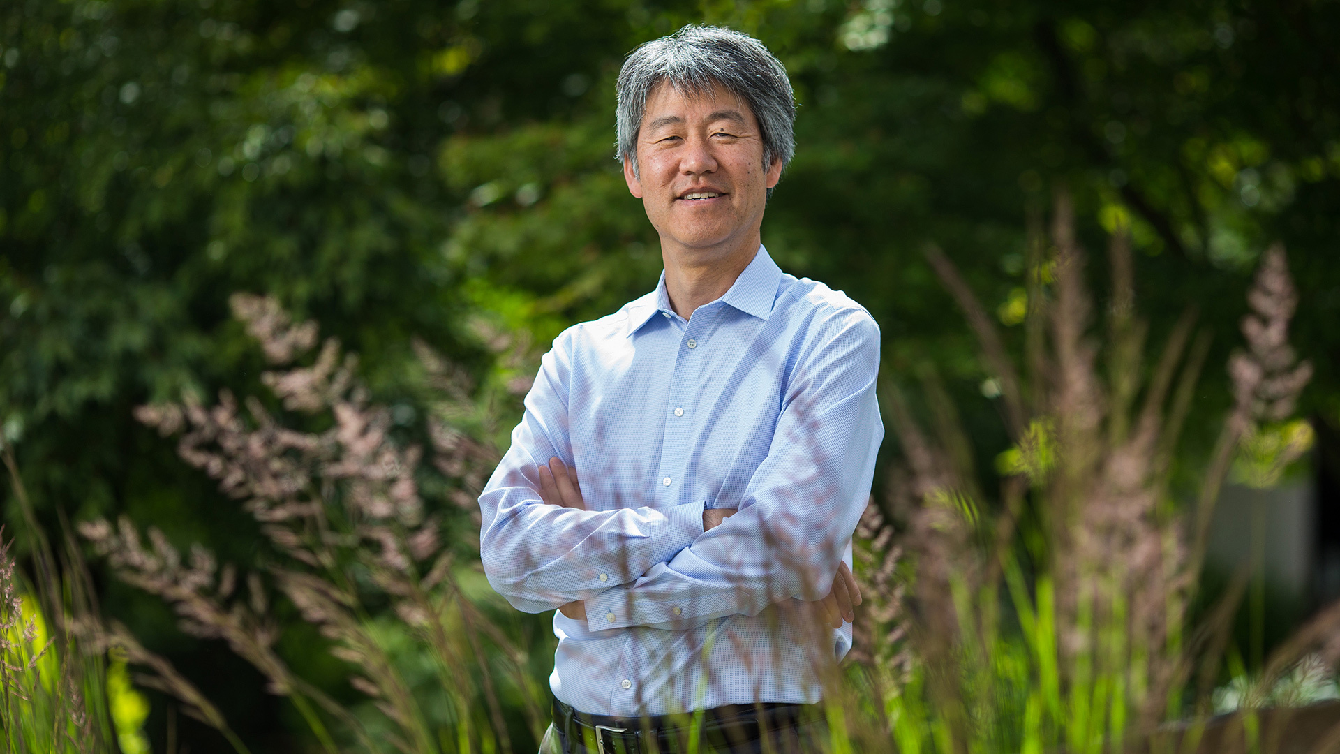 Peter Lee stands with arms crossed behind some plants