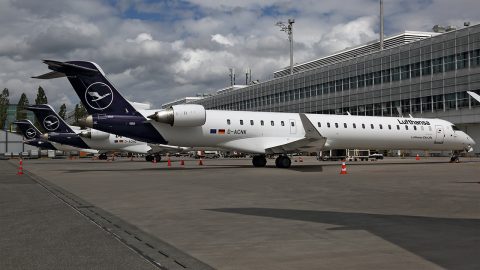 A Lufthansa CityLine airplane is parked on the tarmac of an airport. The tails of two other Lufthansa CityLine airplanes are visible in the background.