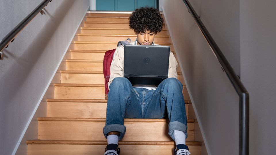 a young person sits on stairs using their laptop
