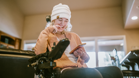 Cheerful woman in wheelchair using a smartphone at home.