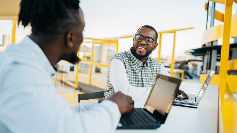 Two men in conversation sitting at laptops outdoors