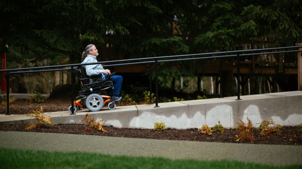 A man using a wheelchair moves up an outdoor ramp.