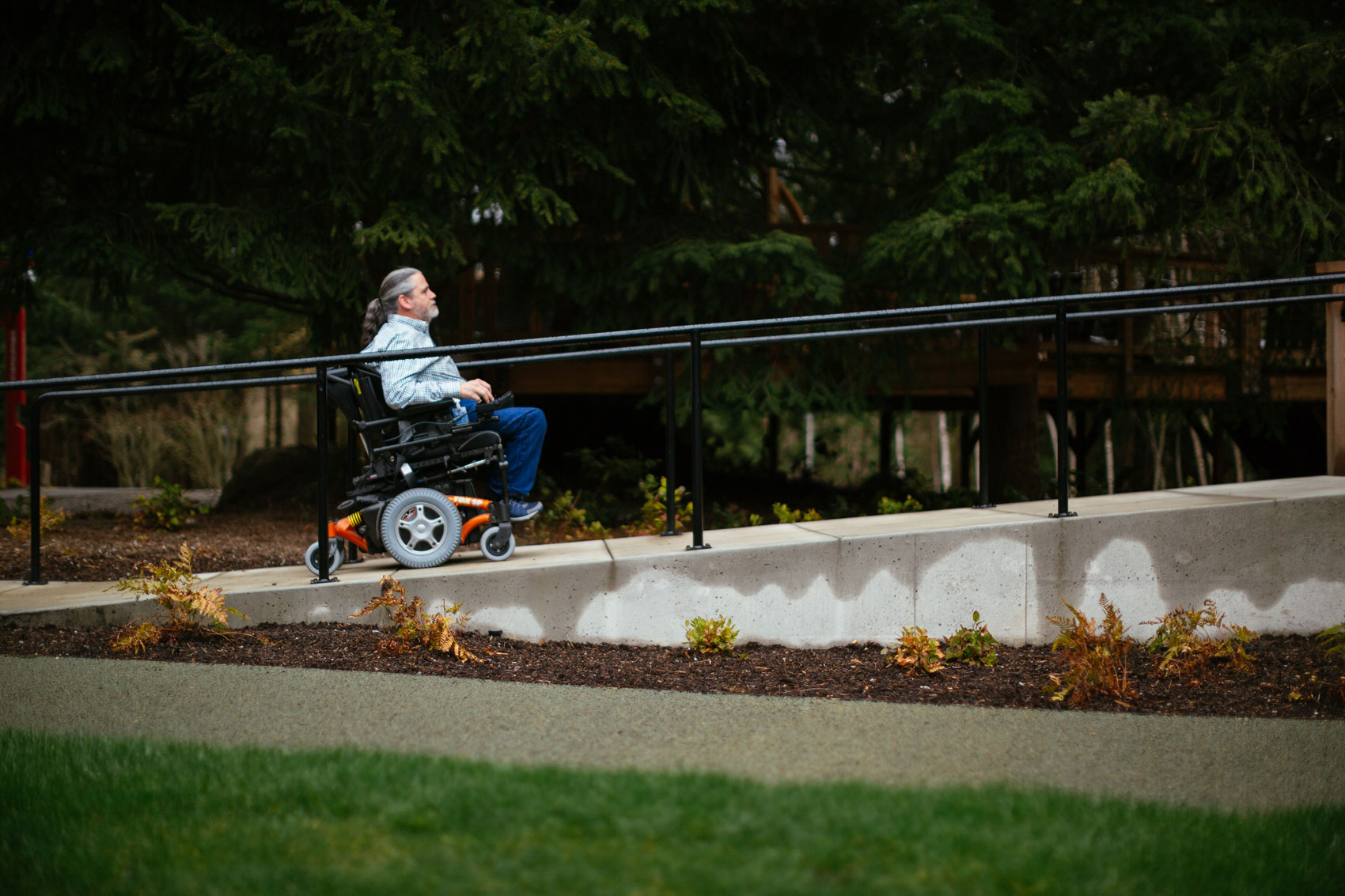 A man using a wheelchair moves up an outdoor ramp.